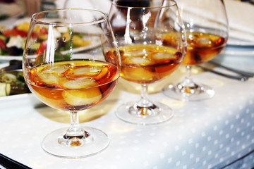 Three glasses of whiskey or cognac with ice on a server tabletop