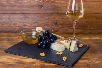 Camembert cheese, nuts, honey and sweet grapes on the background of a glass of white dry wine