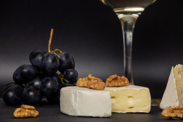 Close-up chopped camembert cheese, nuts and sweet blue grapes on the background of a glass of white dry wine