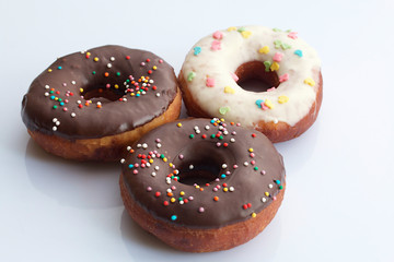 American donuts, glazed with melted chocolate and decorated with sprinkling, lie on a platter.