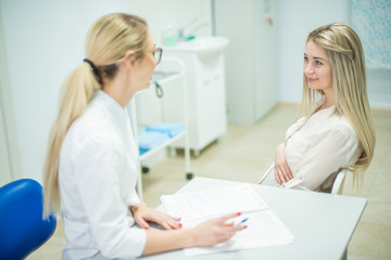 Fototapeta premium Young pregnant woman taking consultation at doctor's office. Beautiful gynecologist and young pregnant woman meet in hospital