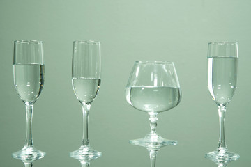 Four glasses filled with water, standing on a table, on a gray background.
