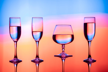 Four wine glasses of water are on the table, behind a colorful background.Glasses reflected in the glass.