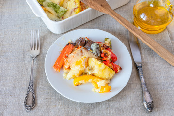 Vegetables baked with cheese in a white plate on a rustic background, top view - vegetable casserole