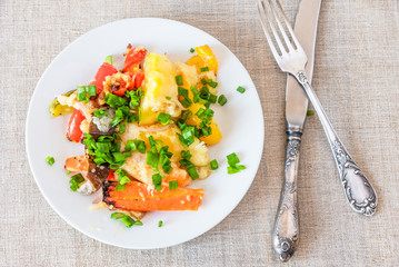 Vegetables baked with cheese in a white plate on a rustic background, top view - vegetable casserole