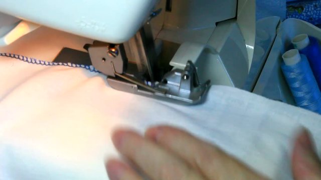 Sewing at home. Processing the edges of white fabric with a finishing seam with blue threads on an overlock machine. Household. Close-up