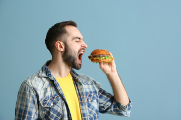 Man eating tasty burger on color background