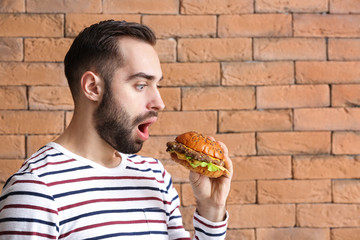 Surprised man with tasty burger against brick wall