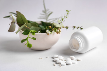 Bottle with pills and herbs on light background