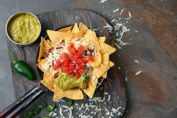 Frying pan with tasty nachos, minced meat, salsa and guacamole on wooden board