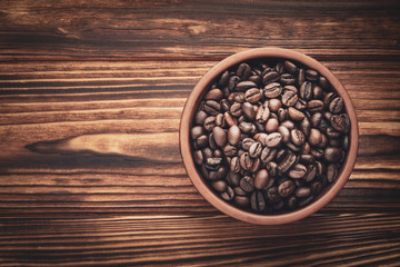 Top view roasted coffee beans in a clay bowl on a wooden background