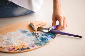 Close up of woman's hand mix paints with brush in palette in art-class