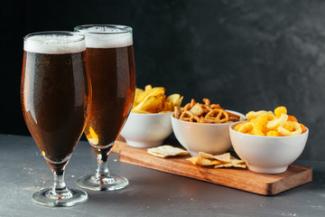 Glass of lager beer with snack bowls on dark stone background