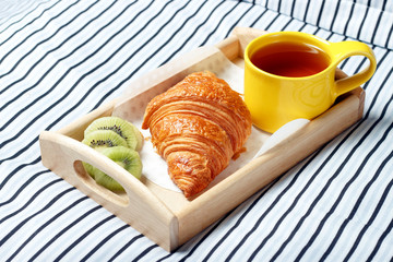 Breakfast in bed, Wooden tray with tea, croissant and fruit