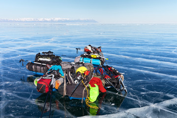 Obraz premium A pile of tourist equipment: tents, backpacks, mats, protective helmets, skates on beautiful blue ice against the boundless ice expanses of the frozen Lake Baikal. Winter tourism concept