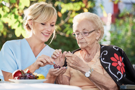 Pflegerin hilft Seniorin beim sch&auml;len von Obst