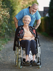 Pfleger mit Seniorin im Rollstuhl im Park unterwegs