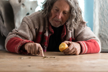 Senior homeless man eating an apple counting coins