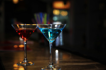 Two martini glasses filled with a colored cocktails standing on the bar counter.