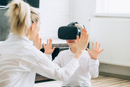 Beautiful blond happy mother playing with her son while using virtual reality headsets at home. Choice entertainment concept.