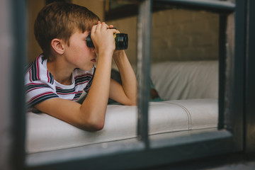 Boy looking outside window using binoculars