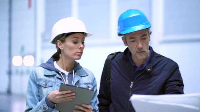 Team of builders and architect looking at blueprint in warehouse