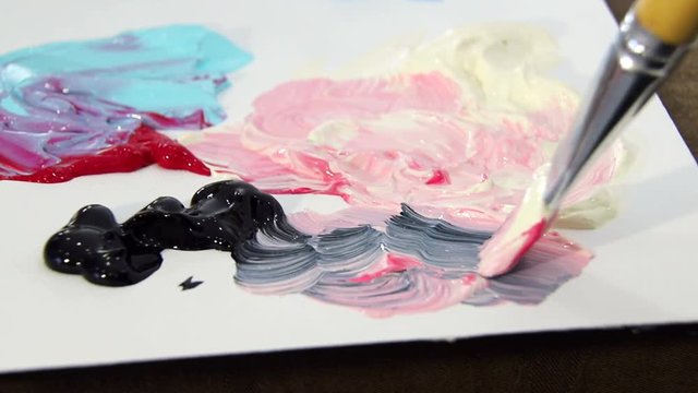 The artist with a brush mixes the ivory, red and black paint on the palette to mix colors. Preparing to draw