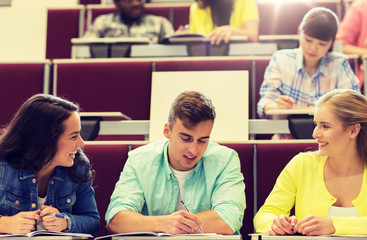 education, high school, university, learning and people concept - group of international students with notebooks writing in lecture hall