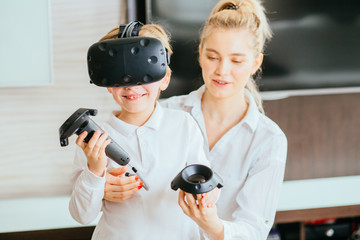 Blond young mother helping her adorable little boy using virtual reality headset at home.