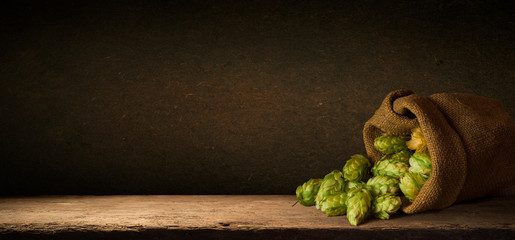Hop twigs frame over wooden cracked table background. Vintage toned. Beer ingredients. Beautiful fresh-picked whole hops with green leaves border design close-up. Brewing concept, Vertical image