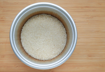 Raw Thai local jasmine rice in pot on wood background ready for cooking.
