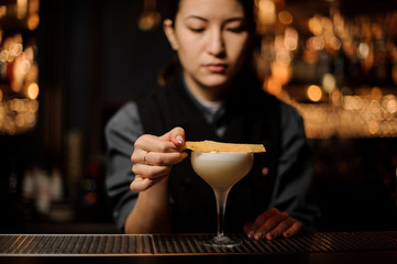 Professional bartender girl adding to a delicious cocktail dried fruit decor