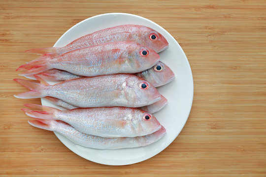 Fresh Ornate threadfin bream on white plate against wooden board background with copy space.