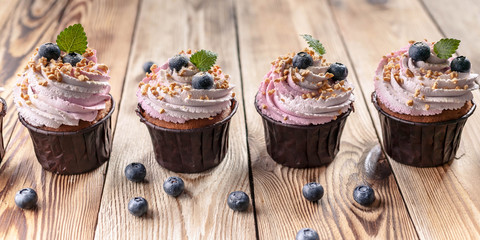 Food banner. Vanilla cupcakes with cream and blueberries on a wooden table.