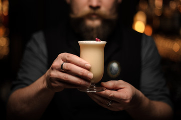 Professional bartender serving a delicious cocktail in the glass decorated with a one red rose bud