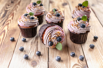Vanilla cupcakes with cream and blueberries on a wooden table.