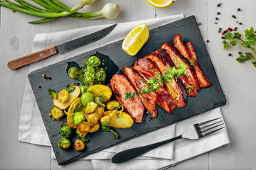 Hanger medium-rare stake with vegetables garnish on a white wooden table. Delicious dinner on a stone board. Top view above.