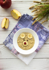Creative idea for kid breakfast - oatmeal porridge with fruits and berries on a white wooden background . Healthy and fun food for kids.