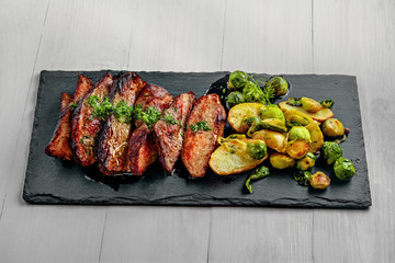 Hanger medium-rare stake with vegetables garnish on a white wooden table. Delicious dinner on a stone board.
