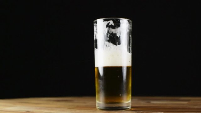 Half empty or half full glass of beer. Rotating on wooden table. Black background with space for text.