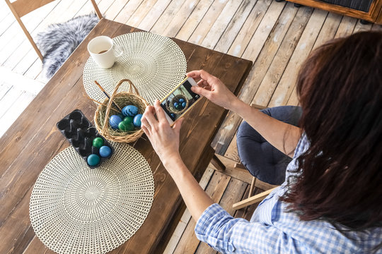 Easter holiday: a girl photographs on a smartphone a basket with colored eggs on the kitchen table.