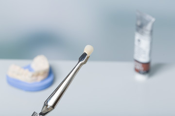 Close up of denture in tweezers in a dental laboratory with imprint in background