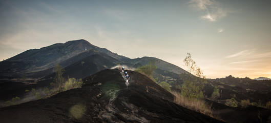 Three friends racing on dirt enduro motorcycles on the black lava at sunrise on mount Batur, Bali, Indonesia