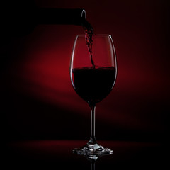 Naklejka na ściany i meble Pouring red wine from a bottle into a wine glass on a black background. Close-up studio shot.