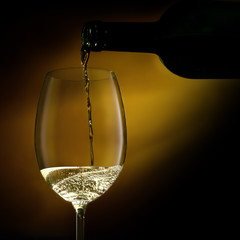 Wine glass is filling with white wine from a bottle.Close-up studio shot on a dark background.