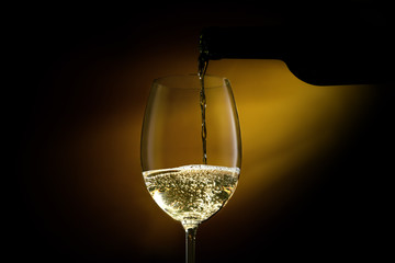 White wine pouring in a glass from a bottle. Studio shot on black background. CLose-up shot.
