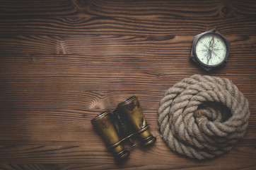 Fototapeta na wymiar Travel or adventure flat lay background with a copy space. Binoculars, mooring rope and a compass on a wooden table.