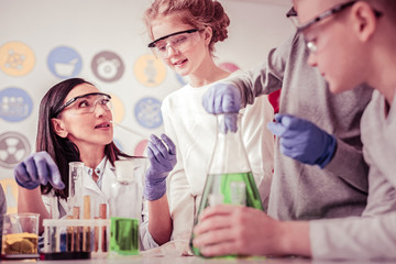 Long-haired woman experimenting with chemicals with students nearby