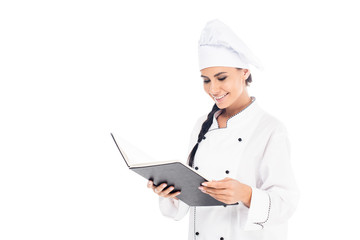 Smiling chef in hat reading cookbook isolated on white