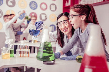 Beaming long-haired teacher mixing liquids in big bulb
